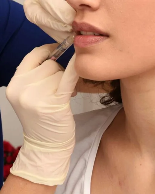 Le mani guantate della dottoressa e la siringa sottile accanto alle labbra